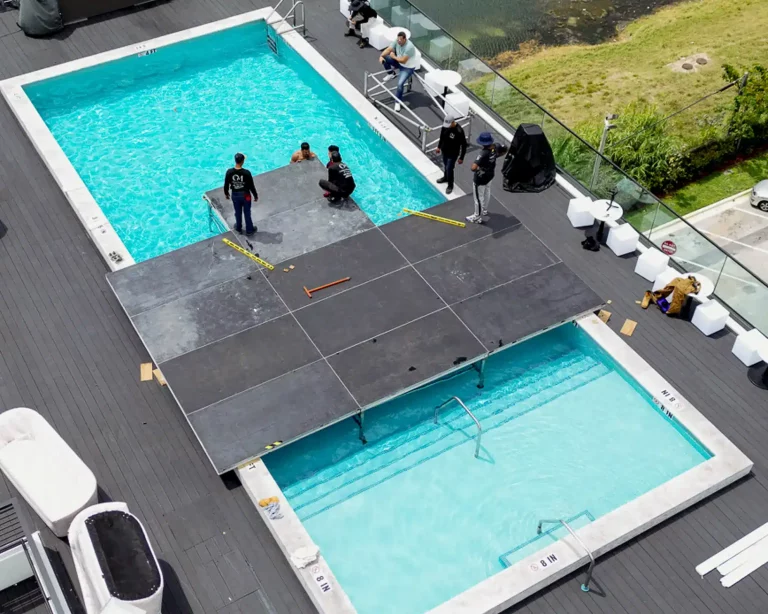 Event crew installing a black pool cover dance floor over a rooftop swimming pool for a corporate event